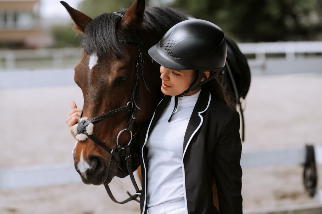 Young female rider in competition attire gently connecting with her horse
